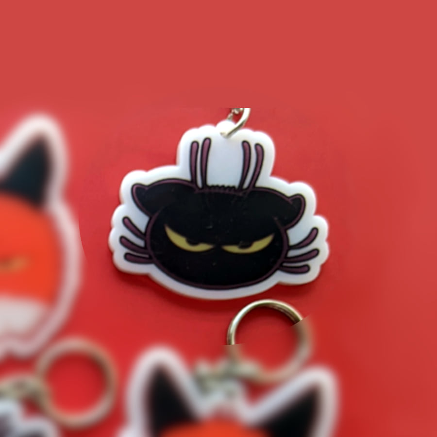 A photo of a charm made of opaque white acrylic. There design is a cat with an angry expression.