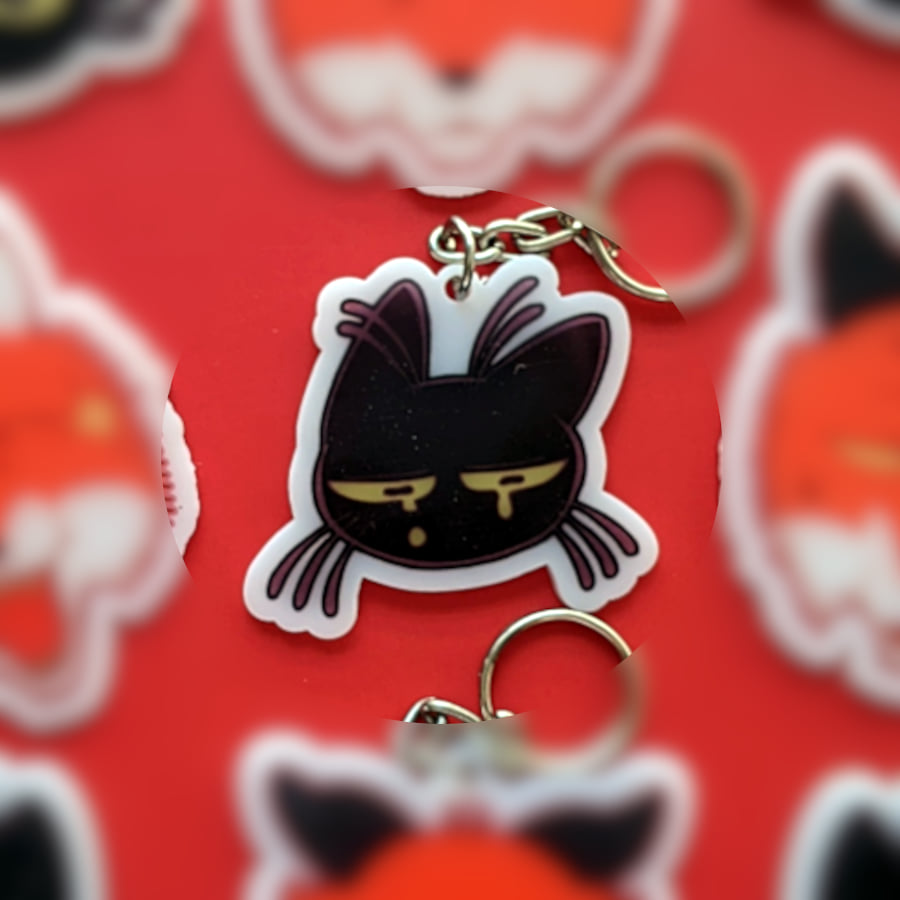 A photo of a charm made of opaque white acrylic. There design is a sad crying cat.