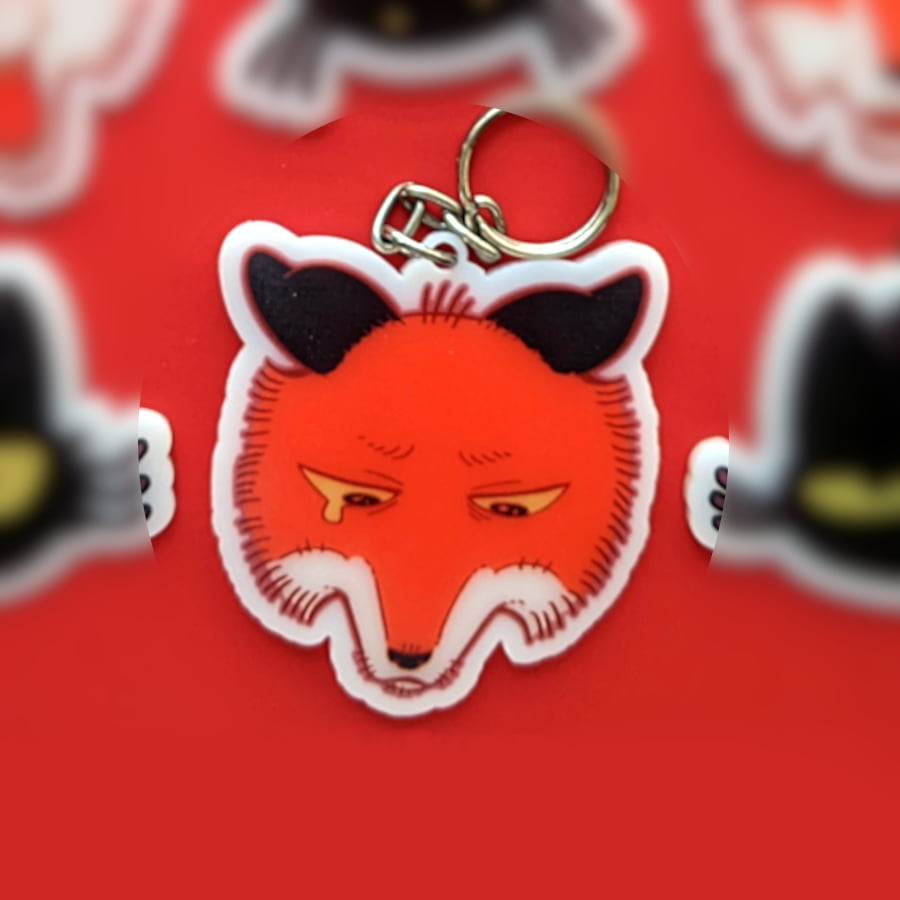 A photo of a charm made of opaque white acrylic. There design is a sad crying fox.