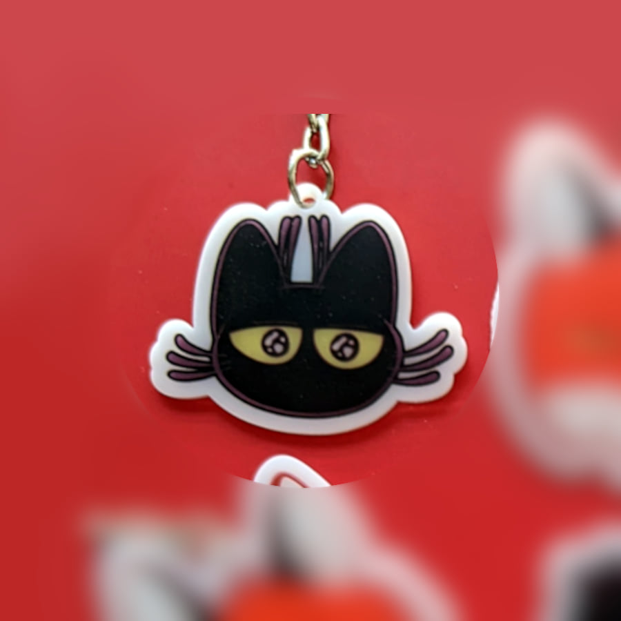 A photo of a charm made of opaque white acrylic. There design is a cat with an excited expression.