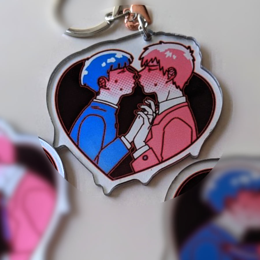 A photo of a charm made of see-through acrylic with a solid silver coating as background color. The design is of two characters, holding hands and ready to kiss.