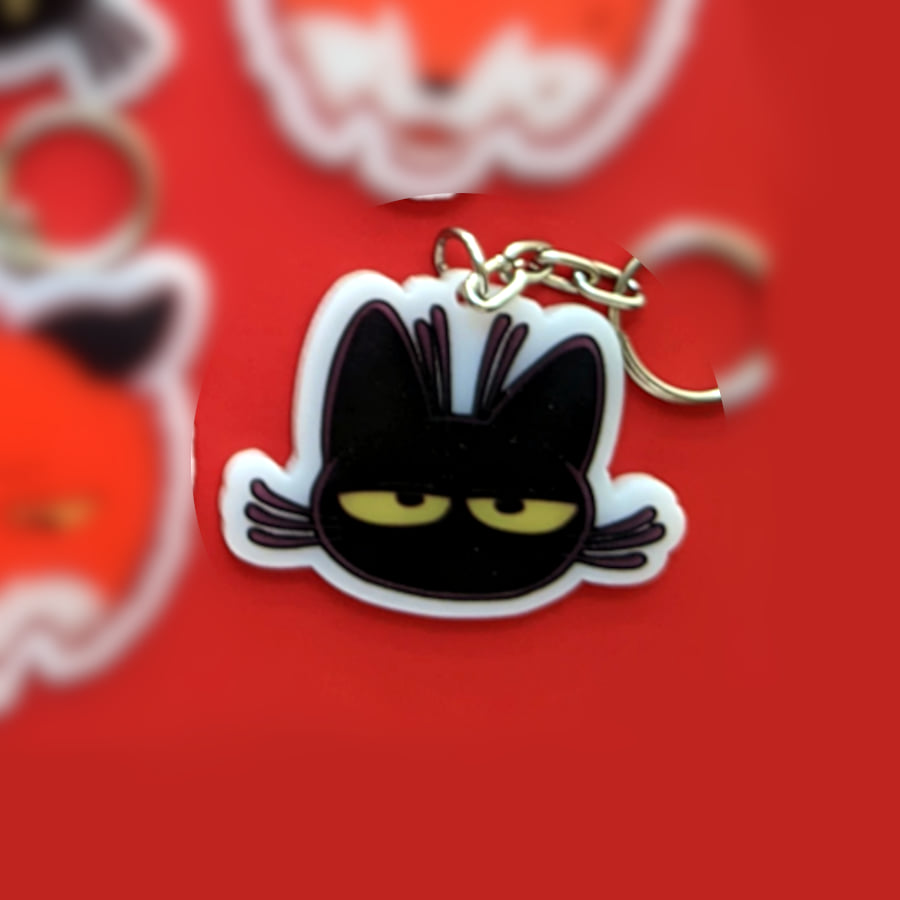 A photo of a charm made of opaque white acrylic. There design is a cat with a blank expression.