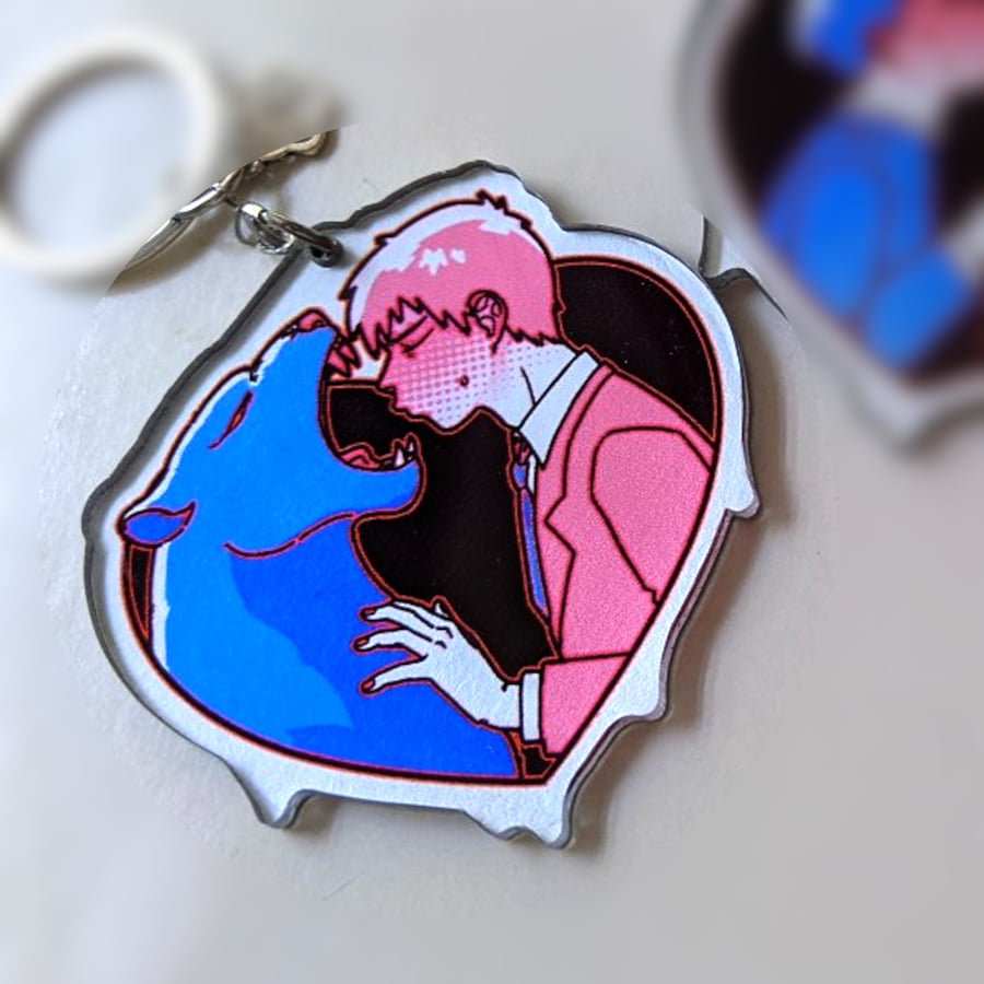 A photo of a charm made of see-through acrylic with a solid silver coating as background color. The design is of two characters, a panther and a human. The human character has his eyes closed, leaning for a kiss. The panther is ready to take a bite of his face.