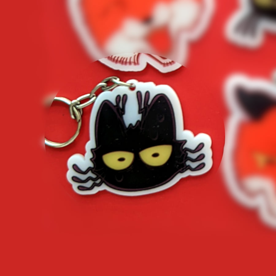 A photo of a charm made of opaque white acrylic. There design is a scared-looking cat.