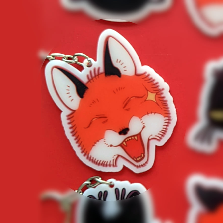 A photo of a charm made of opaque white acrylic. There design is a fox smiling.
