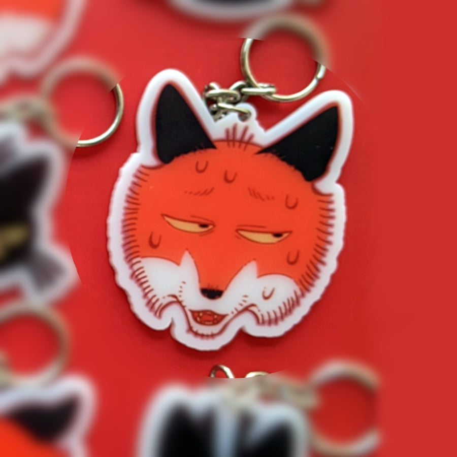 A photo of a charm made of opaque white acrylic. There design is a sweaty nervous fox.